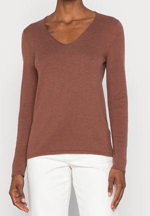 Brauner langärmeliger V-Ausschnitt-Pullover aus weichem Strickstoff, mit tailliertem Schnitt und Rippstrickstruktur, kombiniert mit weißen Hosen.