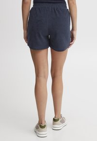 Mørkeblå, myke terry-stoff shorts med elastisk midje, med klassisk snitt og buet hem. Kombinert med lyse treningssko.