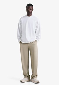 Bela srajca z dolgimi rokavi, bež hlače, lahki supergi. Preprost dizajn, sproščen kroj, mehka tkanina in minimalističen stil.