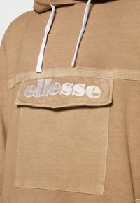 Hoodie marron avec une grande poche avant arborant un logo "ellesse" en argent. Le tissu est doux, avec des cordons blancs sur la capuche.