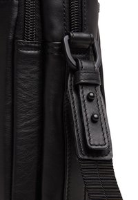 Schwarze Ledertasche mit glatter Textur, robusten Reißverschlüssen, verstellbarem Tragegurt mit genietetem Akzenten und gesteppten Details.