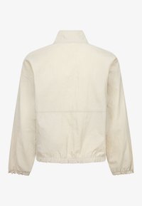 Veste légère de couleur crème dotée d'un col montant, de poignets élastiques et d'un ourlet froncé. Tissu texturé avec des coutures minimales.
