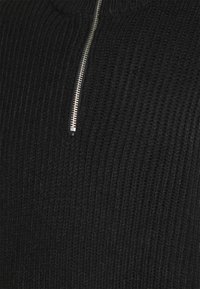 Pull noir en tricot avec une texture en côtes verticales et une fermeture éclair argentée au niveau du cou.