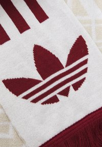 Rød og hvid strikket tørklæde med tre lodrette røde striber, et stort rødt adidas-logo og frynser i den ene ende.