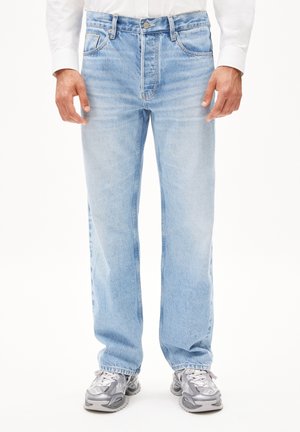 Jeans de mezclilla en azul claro con un diseño de pierna recta, con un lavado desteñido, bolsillos frontales y cierre de botón. Combinados con zapatillas deportivas grises.