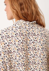Camicia leggera con una base bianca e un motivo astratto multicolore nei toni del nero, arancione e bordeaux, con colletto classico.