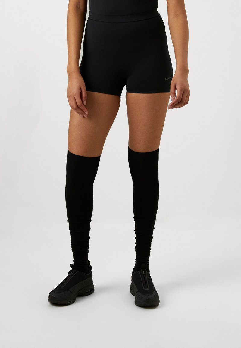Pantalones cortos deportivos negros con una cintura alta, combinados con calentadores de piernas negros hasta la rodilla y zapatos de deslizar negros con cierre de cremallera.
