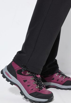 Mustat ulkoiluhousut yhdistettynä värikkäisiin vaelluskengiin, joissa on pinkki päällinen, harmaa pohja, metalliset nyökit ja tekstuuritetut nauhat.