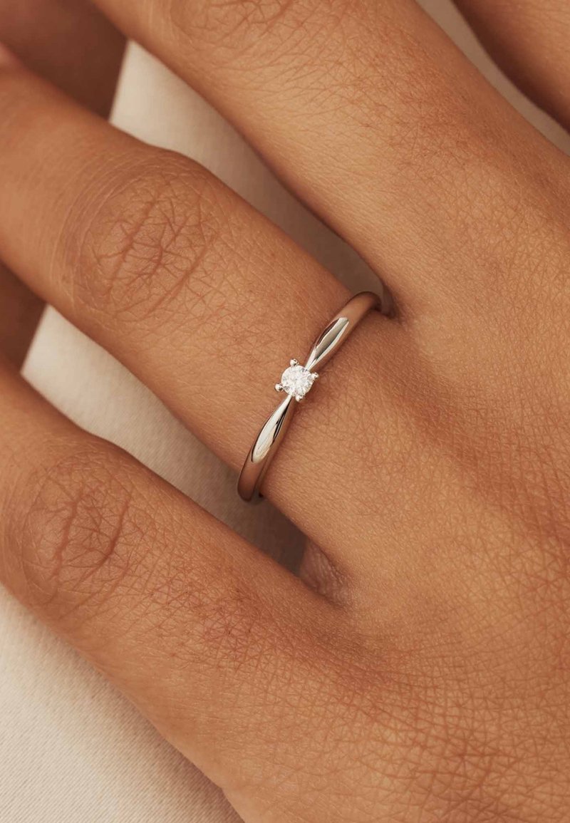 Silberring mit einem gebogenen Band, das einen einzelnen runden Diamanten in zarten Krappen fasst. Sanfte Textur, minimalistisches Design.