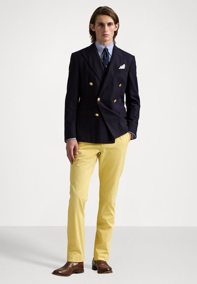 Mornarica s dvostrukim kopčanjem, žute hlače, prugasta ko�šulja, plava kravata i smešene kožne cipele. Blazer ima zlatne dugmadi; detalj maramice u džepu.