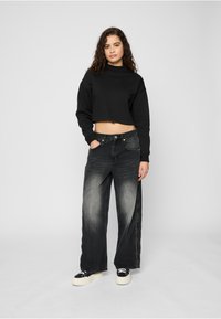 Sort cropped genser med høy hals. Vide svarte jeans med falmet tekstur. Hvite platåsneakers med svarte detaljer.
