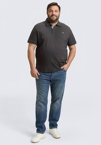 Donkergrijs poloshirt met een kraag, gecombineerd met een blauwe spijkerbroek en witte sneakers. Opvallend logo op de borst en korte mouwen.