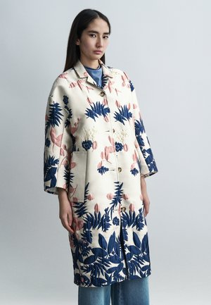 Palton cu model floral în nuanțe de bej, decorat cu motive botanice albastre și roz. Prevăzut cu guler, nasturi și buzunare.