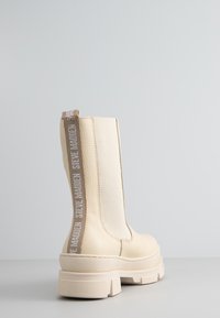 Stivaletto beige con suola spessa, realizzato in pelle e tessuto testurizzati, dotato di un tab posteriore con dettaglio del marchio.