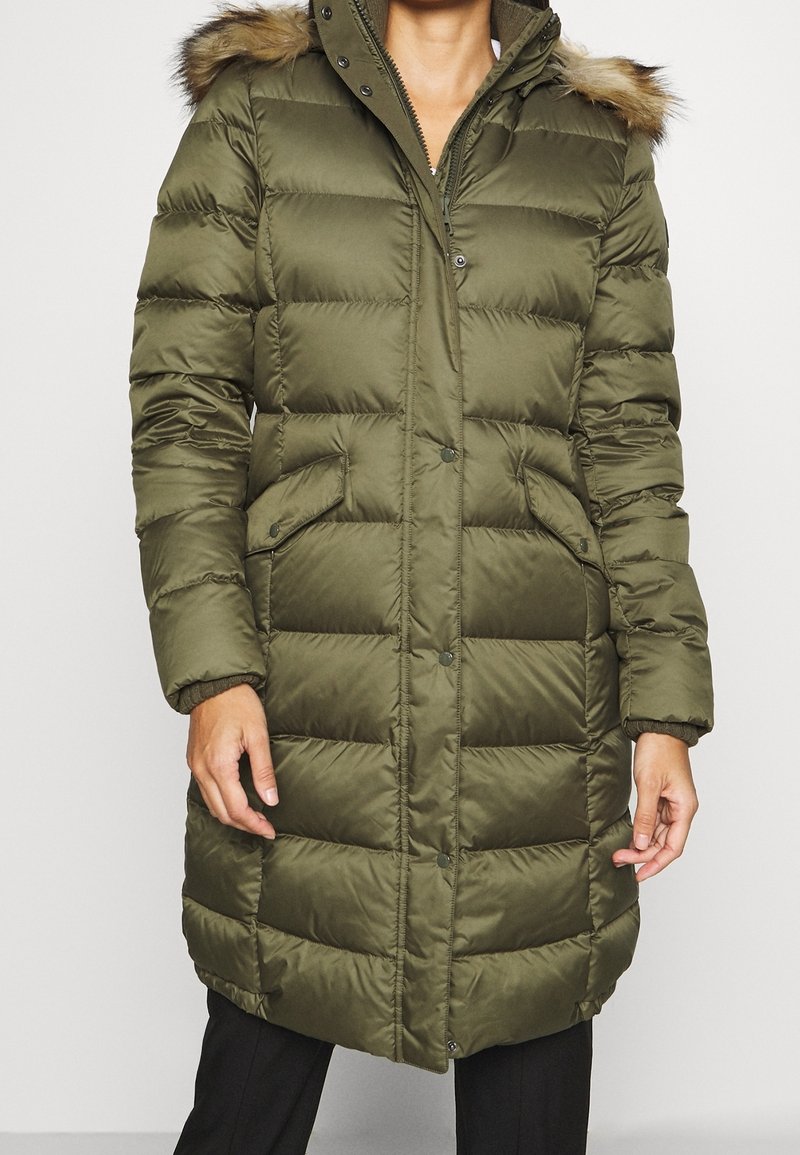 Cappotto imbottito verde oliva con cappuccio e rifiniture in pelliccia sintetica, due tasche frontali e chiusura a bottone a pressione, realizzato in materiale trapuntato.