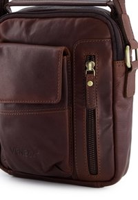 Braun lederschultertasche mit vorderer klappenaußentasche, vertikaler reißverschlusstasche und verstellbarem riemenverschluss auf der rechten seite.