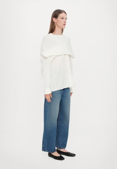 Witte, loszittende top met een gedrapeerde detail bij de hals, gecombineerd met blauwe wijde jeans en zwarte platte schoenen. Eenvoudig en modern design.