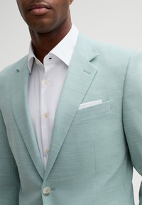 Light blue blazer made of textured fabric, featuring a notch lapel, single button, and a white dress shirt underneath with button details.