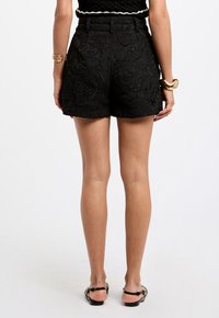 Black lace shorts with a floral pattern, high waist, and hem finishing just above the knee. Worn with simple black sandals.