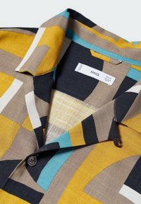 Camisa de manga corta con un patrón geométrico en amarillo, marrón, negro y verde azulado, fabricada con una tela texturizada y cierre de un solo botón.