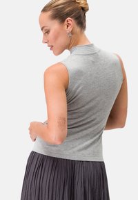 Top grigio senza maniche con colletto alto, realizzato in un tessuto morbido. Presenta una vestibilità aderente, abbinato a una gonna plissettata grigia fluida.
