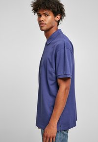 Polo en coton violet foncé, avec un col, des manches courtes et des fentes sur les côtés à l'ourlet pour plus de liberté de mouvement.