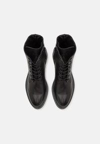 Botas de tobillo de cuero negro con una superficie suave, costuras elevadas, delantero con cordones y cremalleras laterales para ponerse y quitarse fácilmente.