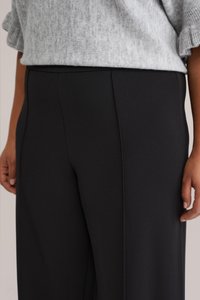 Leveälahkeiset mustat housut, joissa on sileä pinta ja pystysauma, yhdistettynä vaaleanharmaaseen neulepaitaan.