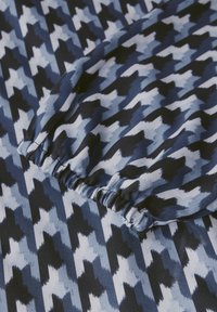 Tissu bleu et noir avec un motif pied-de-poule aux nuances variées de bleu. Le matériau présente un bord froncé le long de la couture.