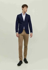 Marinblå blazer med två knappar över en ljusblå skjorta, tillsammans med beige chinos och svarta skor. Slät tyg, skräddarsydd passform och klassisk design.