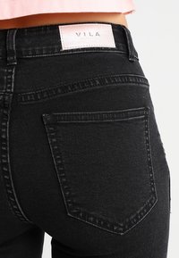 Vaqueros de mezclilla negra de cintura alta, con una etiqueta de VILA en la cintura trasera y un detalle de costura sutil en los bolsillos.