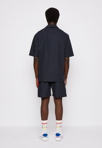 Camicia a maniche corte blu navy e pantaloncini coordinati con vestibilità comoda, caratterizzati da un dettaglio sulla spalla posteriore e cuciture a contrasto. Completano il look calzini bianchi e sneaker.