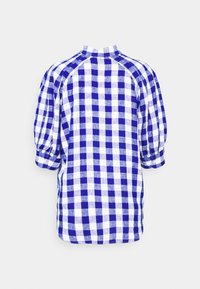 Chemise en vichy bleue et blanche avec un col haut, des manches bouffantes et une coupe ample ; fabriquée en tissu léger avec un motif à carreaux.