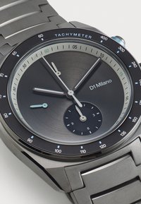 Montre ronde en métal gris avec une échelle tachymétrique, un cadran noir, des index horaires argentés et une finition brossée sur le boîtier et le bracelet.