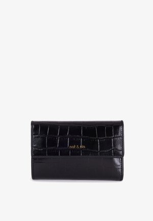 Cartera de cuero negro con estampado de cocodrilo y cierre de solapa, con logotipo dorado. Sostenida en la mano contra un fondo de abrigo beige.