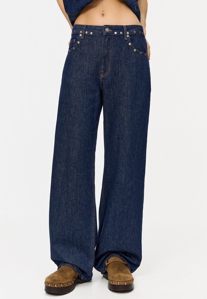 Wide-leg denim jeans in dark blue, featuring metal buttons and contrasting stitching. The fabric has a smooth texture, providing a relaxed fit.
