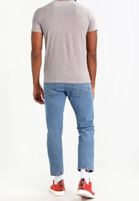 Graues T-Shirt mit kurzen Ärmeln, hellblaue Jeans und rote Turnschuhe mit weißen Sohlen sowie gemusterte Socken, Ansicht von hinten.