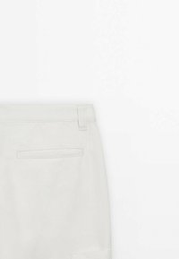 Pantaloni grigi chiari con una texture liscia, dotati di tasca posteriore, passanti per cintura e design sartoriale. Il materiale sembra resistente.