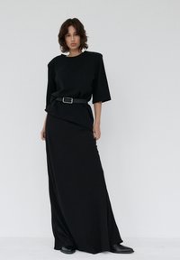 Czarny dwuczęściowy zestaw z krótkim rękawem i asymetrycznym wzorem na górze oraz dopasowaną, długą spódnicą. Look uzupełnia pasek jako akcent.