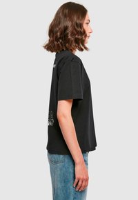 Black cotton t-shirt with a relaxed fit, featuring short sleeves, a rounded neckline, and minimalist white graphic text on the front.