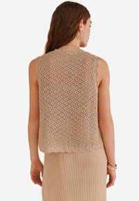 Top en tricot beige sans manches avec un motif en losanges texturé et des bords festonnés, associé à un bas beige côtelé.