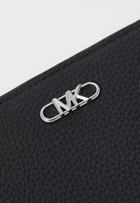 Portefeuille en cuir texturé noir avec un accent en métal argenté au logo MK. Le design inclut un fermoir lisse et arrondi pour une fermeture sécurisée.