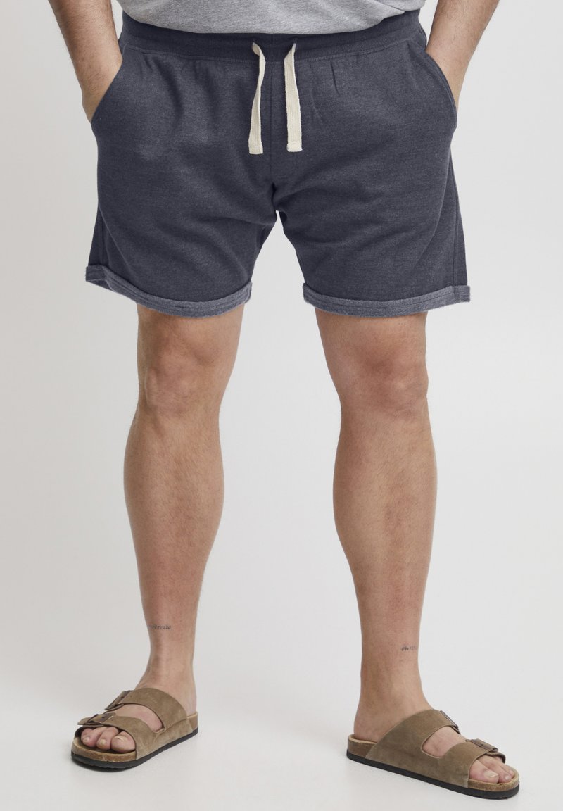 Grå bomullsshorts med rullekanter og elastisk liv, med beige snøring og sidelommer, paret med brune sandaler.