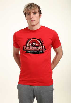 Giovane uomo che indossa una maglietta rossa con una grafica di Deadpool e la scritta "DOGPOOL" e "Non insultare l'autonomia di questo animale."