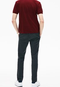 Chemise bourgogne à manches courtes associée à un pantalon à carreaux sombre et des baskets blanches, mettant en valeur une coupe décontractée et moderne ainsi qu'un tissu léger.