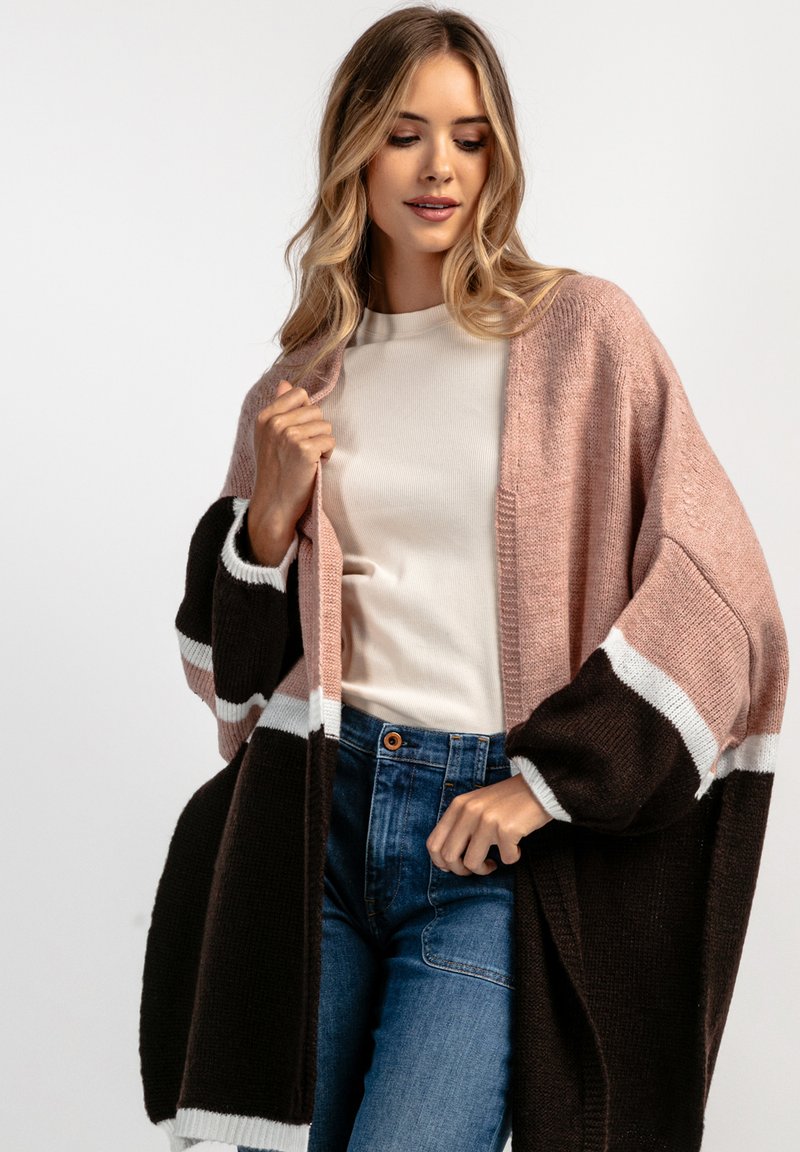 Sweter kardigan w kolorach różowym, brązowym i białym; oversize'owy krój z szerokimi rękawami; warstwowa tekstura; w połączeniu z kremową bluzką i niebieskimi dżinsami.