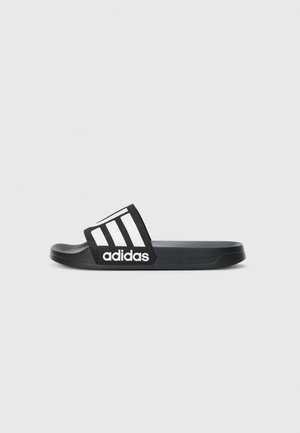 Sandale en plastique noir Adidas avec le logo trois bandes blanches sur la bride, semelle plate et semelle texturée sur un fond clair.
