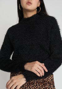 Svart fluffig tröja med långa ärmar och hög halsringning, bärs över en leopardmönstrad kjol, med en mjuk, texturerad yta.