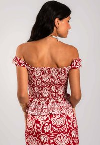 Top de hombros descubiertos con estampado floral en rojo y blanco, con textura fruncida y mangas con volantes, que cuenta con un dobladillo peplum y patrones intrincados.