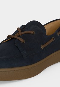 Mocassin en daim bleu marine avec lacets en cuir marron et œillets, avec une semelle épaisse en caoutchouc marron.
